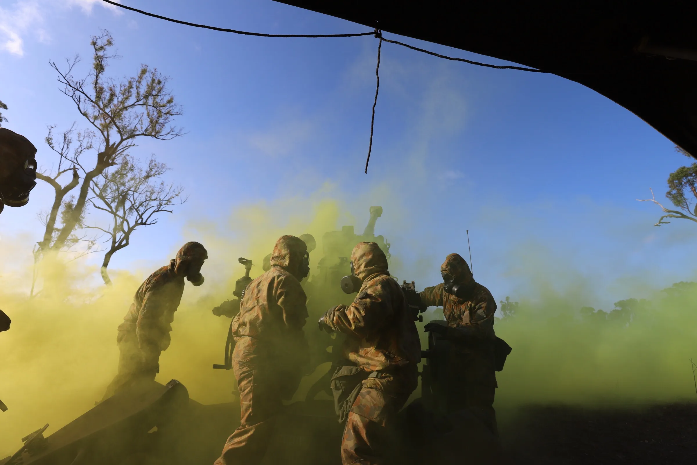 Soldiers advancing on foot through coloured screening smoke during a field training exercise.