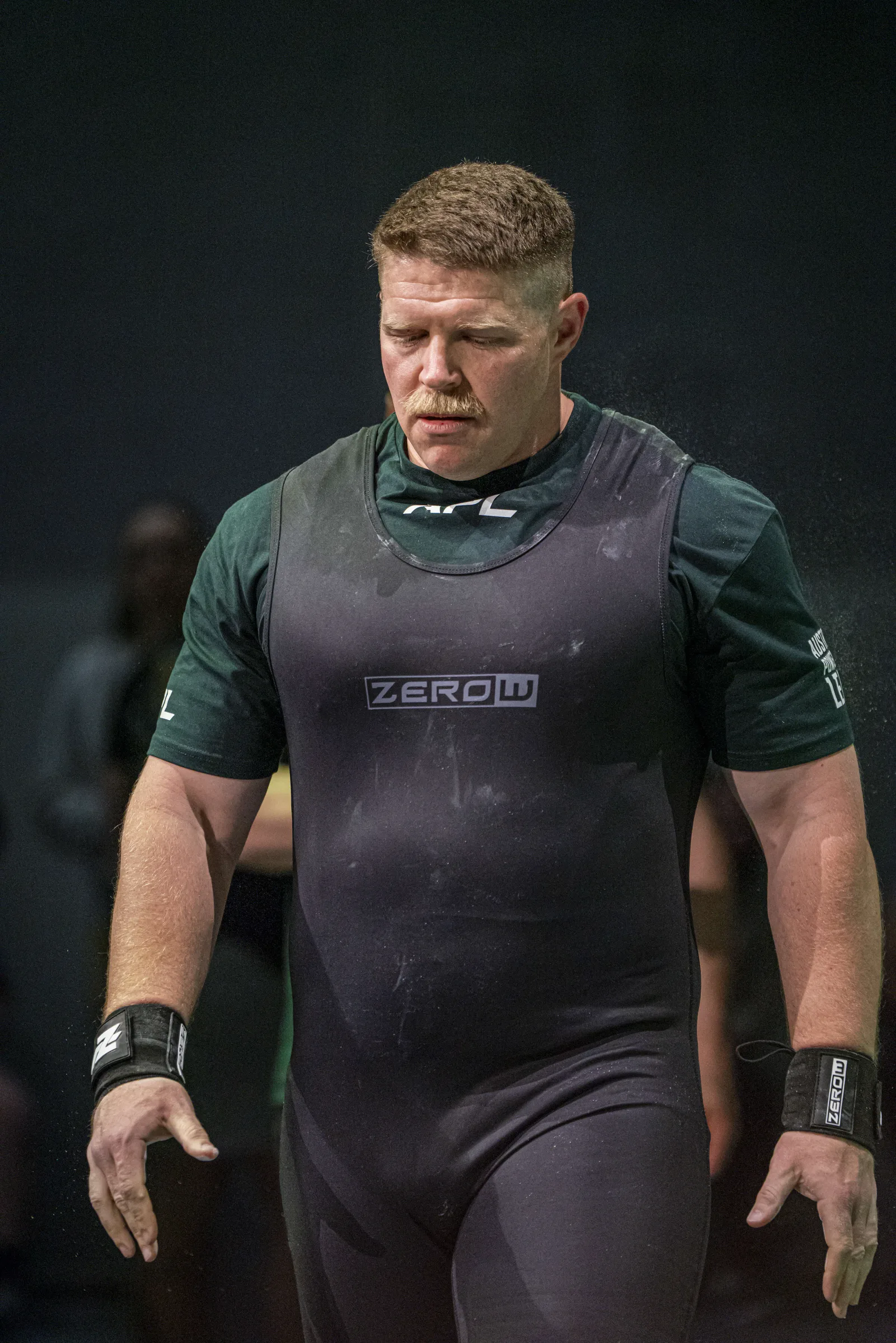 Abe Dearmer standing on the competition platform in a singlet and belt, waiting to lift.