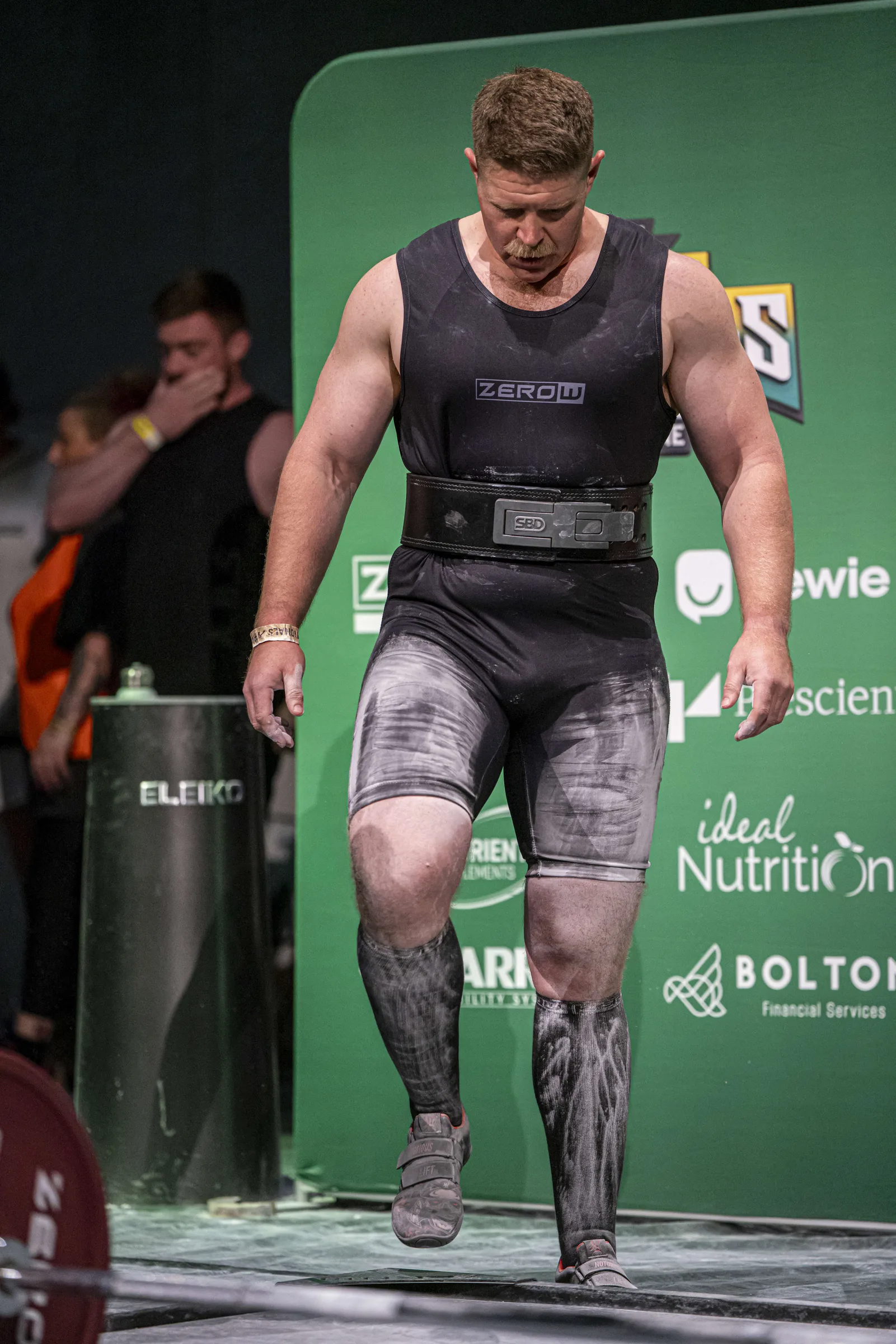 The coach walking out of the rack under a loaded bar, mid-competition.