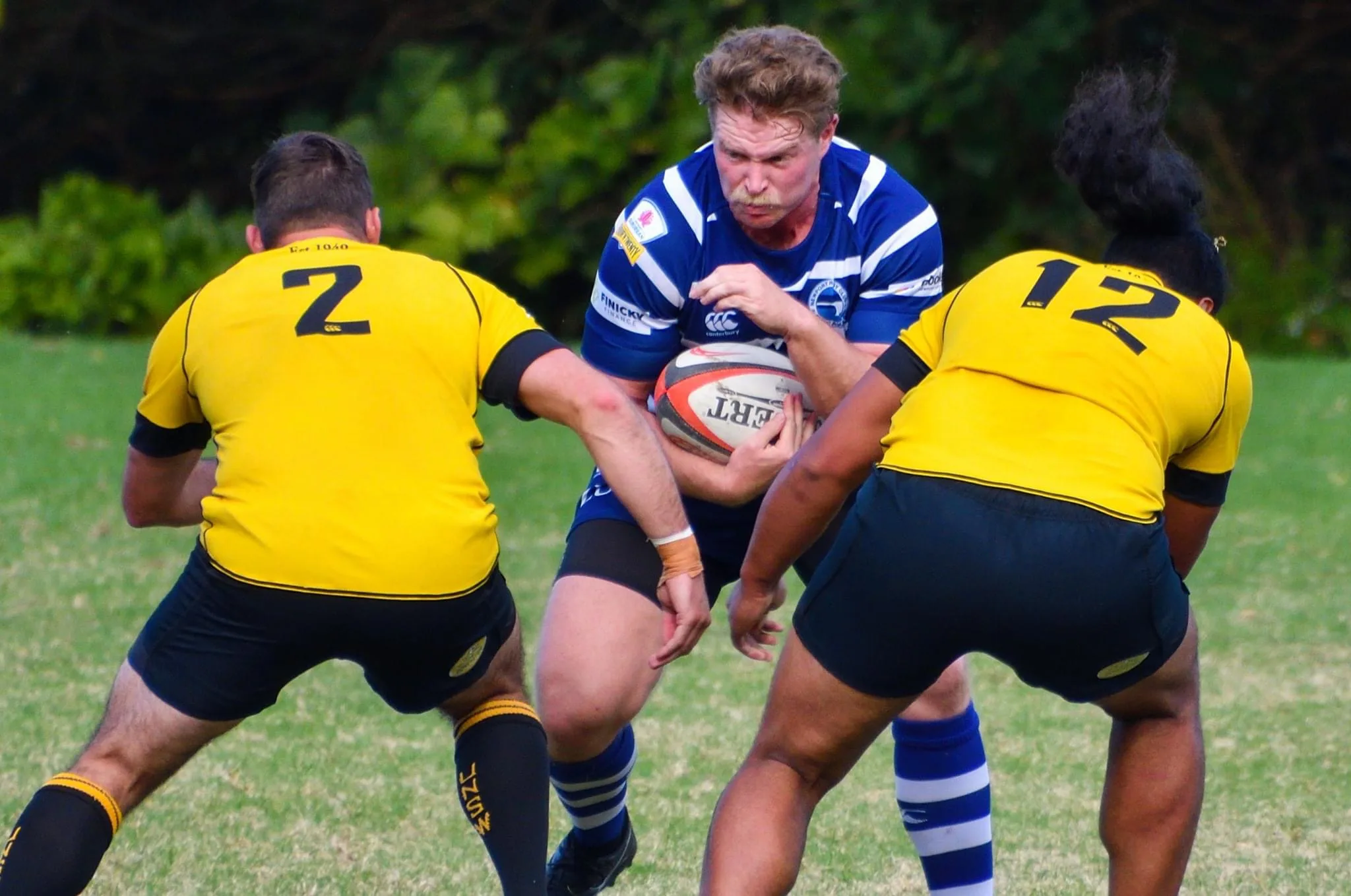 A ball carrier stepping into two defenders during a club rugby fixture.