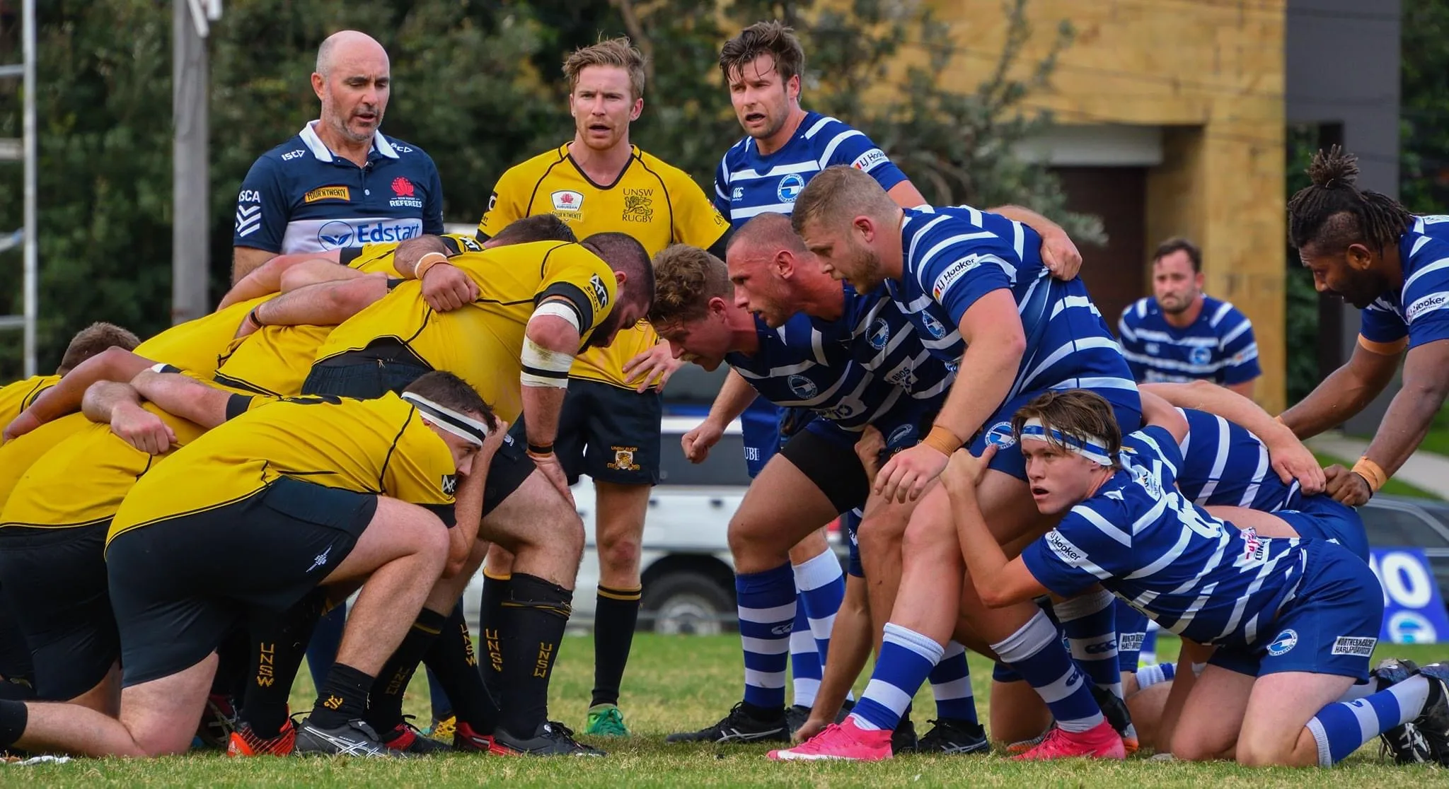 Two club rugby front rows packing down into a scrum on a grass pitch.